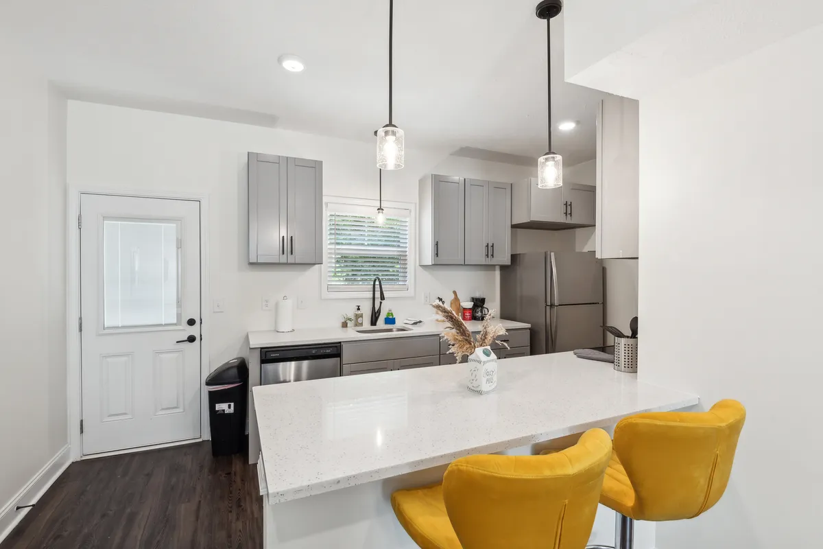 A modern kitchen area featuring a granite countertop, bold yellow bar stools, sleek cabinetry, and high-end appliances. The inviting design suggests easy meal preparation and opportunities to gather or entertain.
