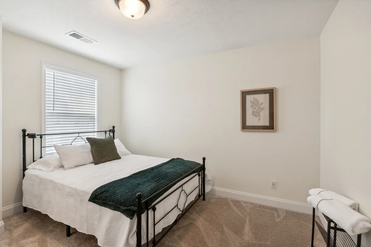 A spacious, sunlit bedroom with a neatly made bed, framed artwork on the walls, and a large window letting in natural light. The room exudes a cozy and serene atmosphere, inviting families to relax and recharge after a day of adventure.