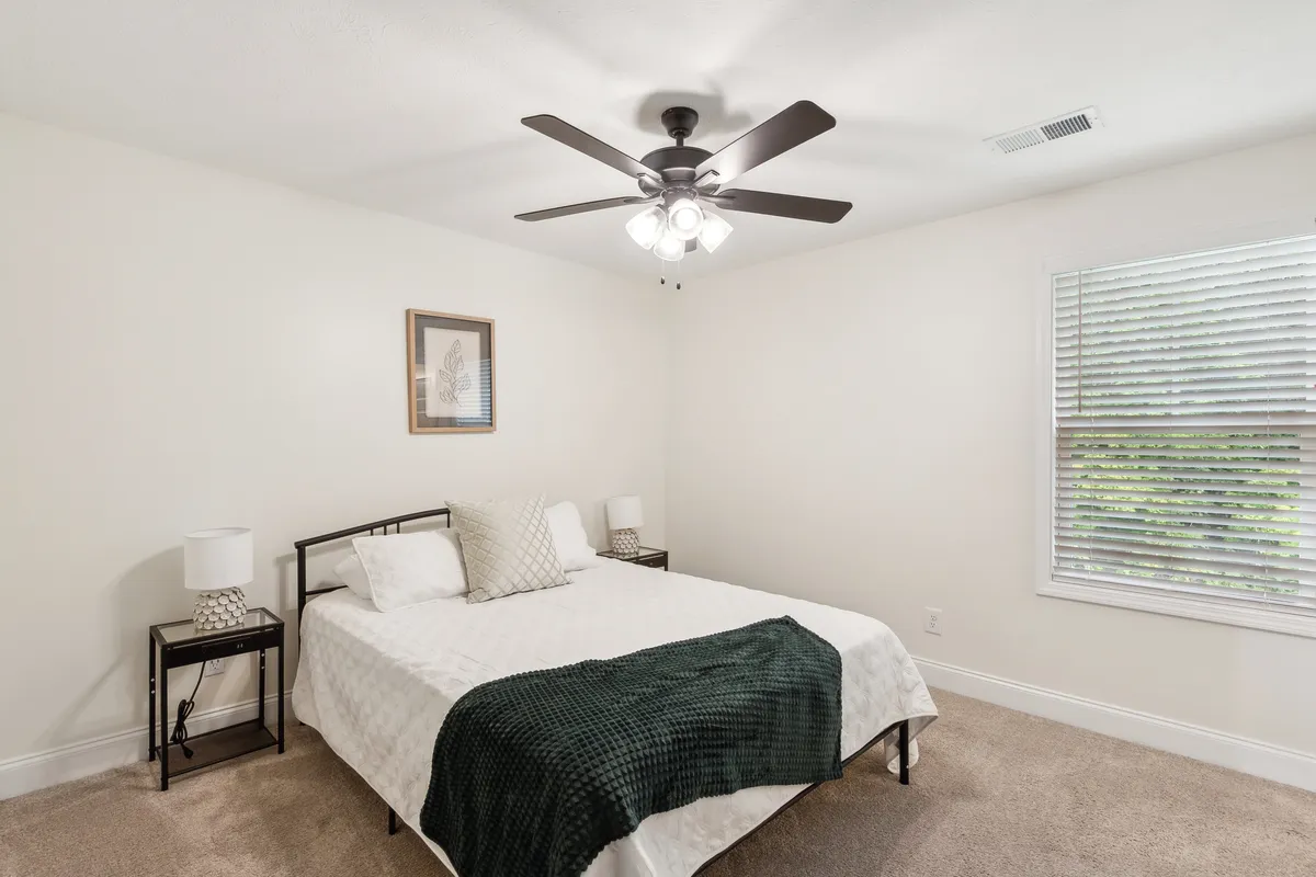 A cozy bedroom featuring a plush bed flanked by nightstands, a ceiling fan overhead, and tasteful wall art. The soft lighting and inviting decor create an atmosphere perfect for relaxation and rest.